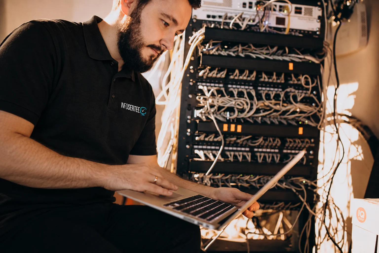Fotografía adaptada: técnico con uniforme de Infosertec trabajando junto a equipos de red